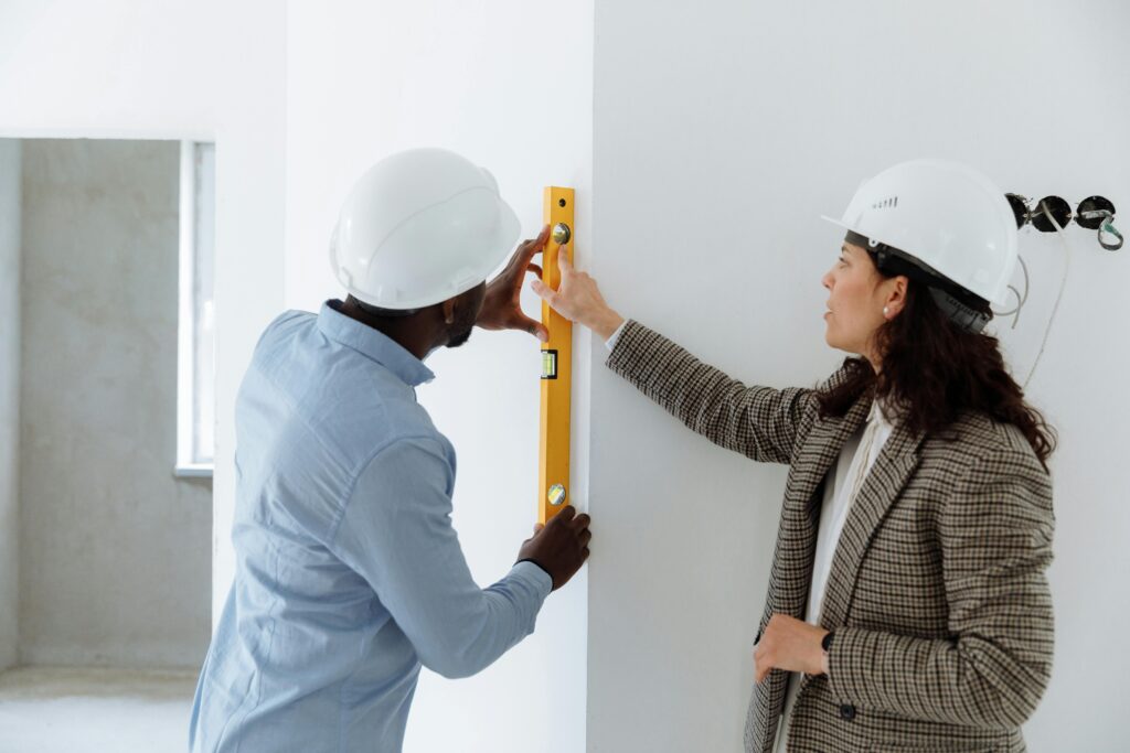 Two contractors using a level bar to check wall alignment inside a building.